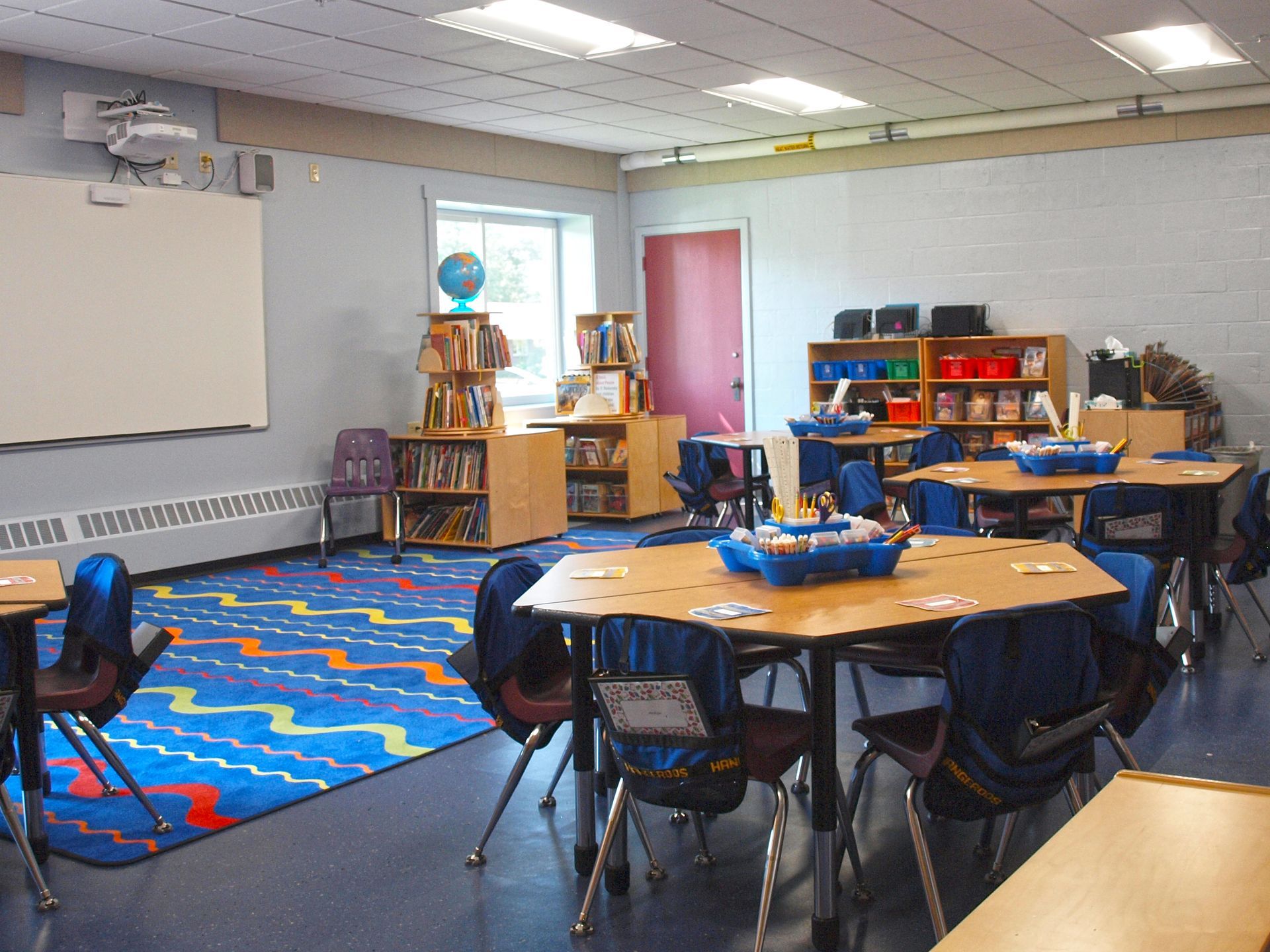 A classroom with tables and chairs and a globe on the wall