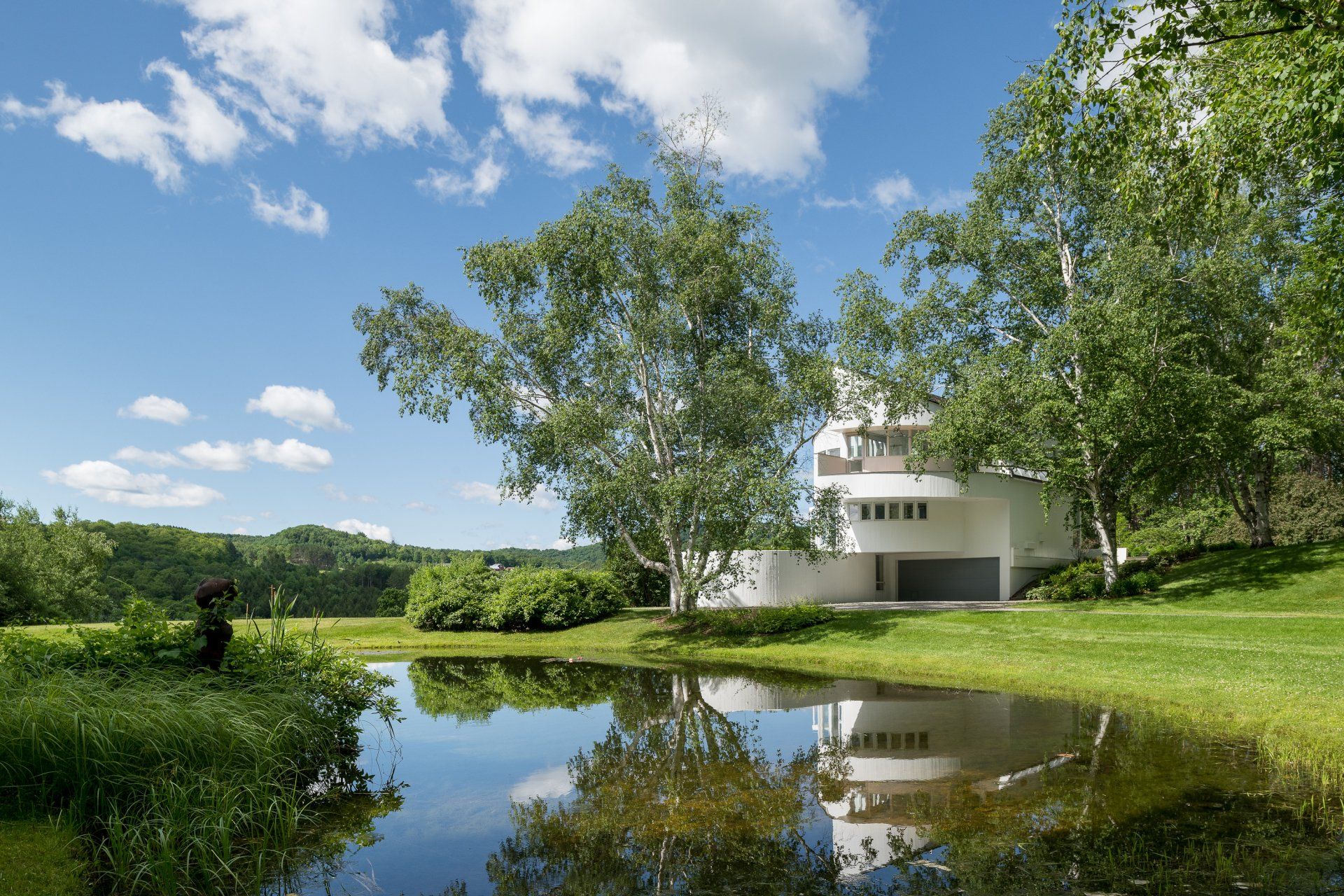 A house is surrounded by trees and a pond in front of it.