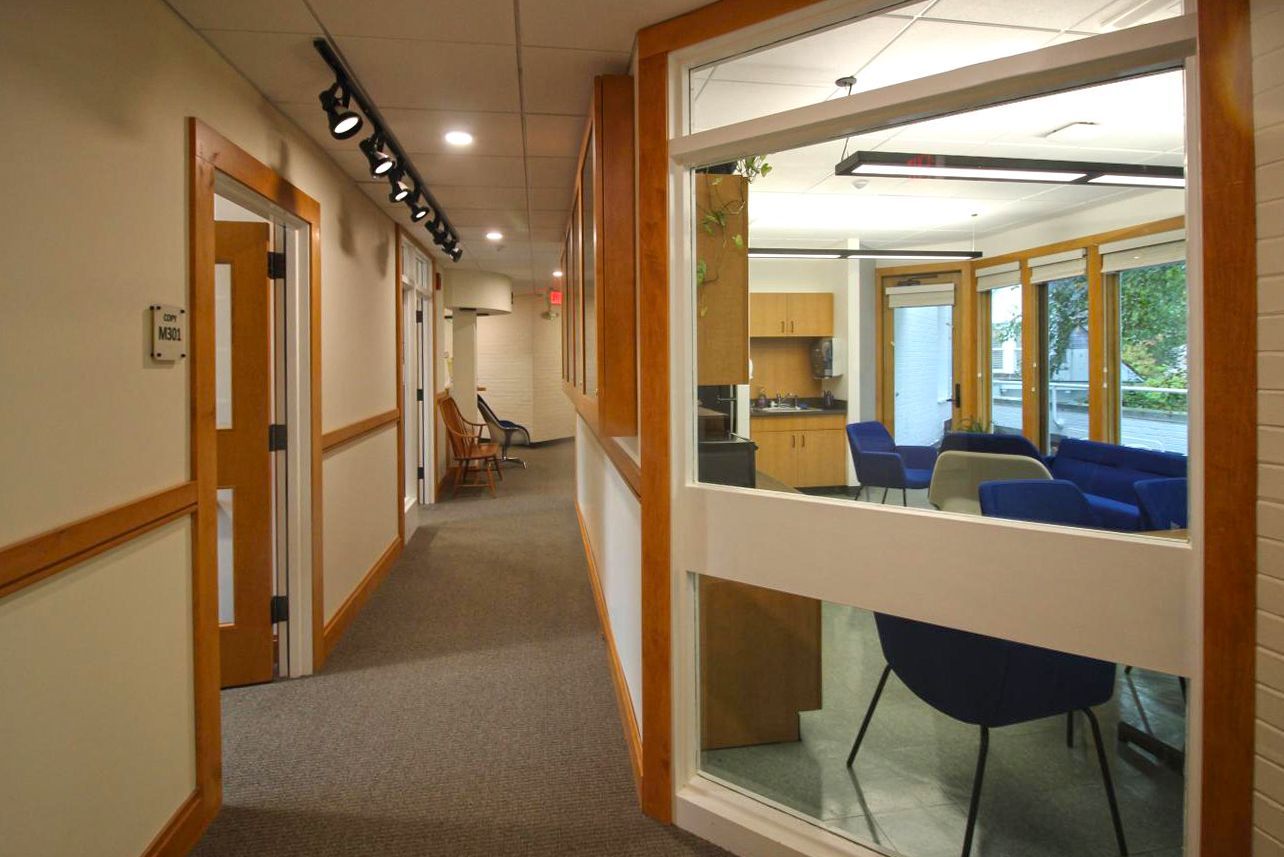 A hallway in a building with a window and chairs.