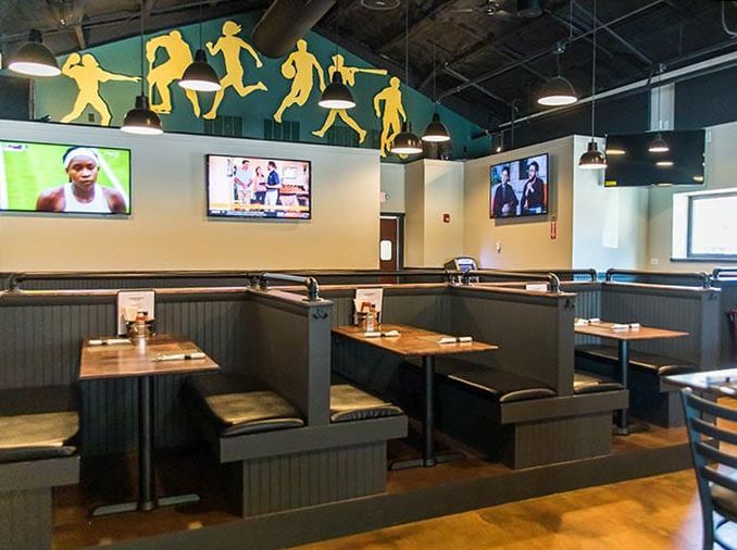 A restaurant with tables , booths , and televisions on the wall.