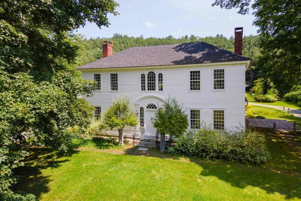 A large white house is surrounded by trees and grass
