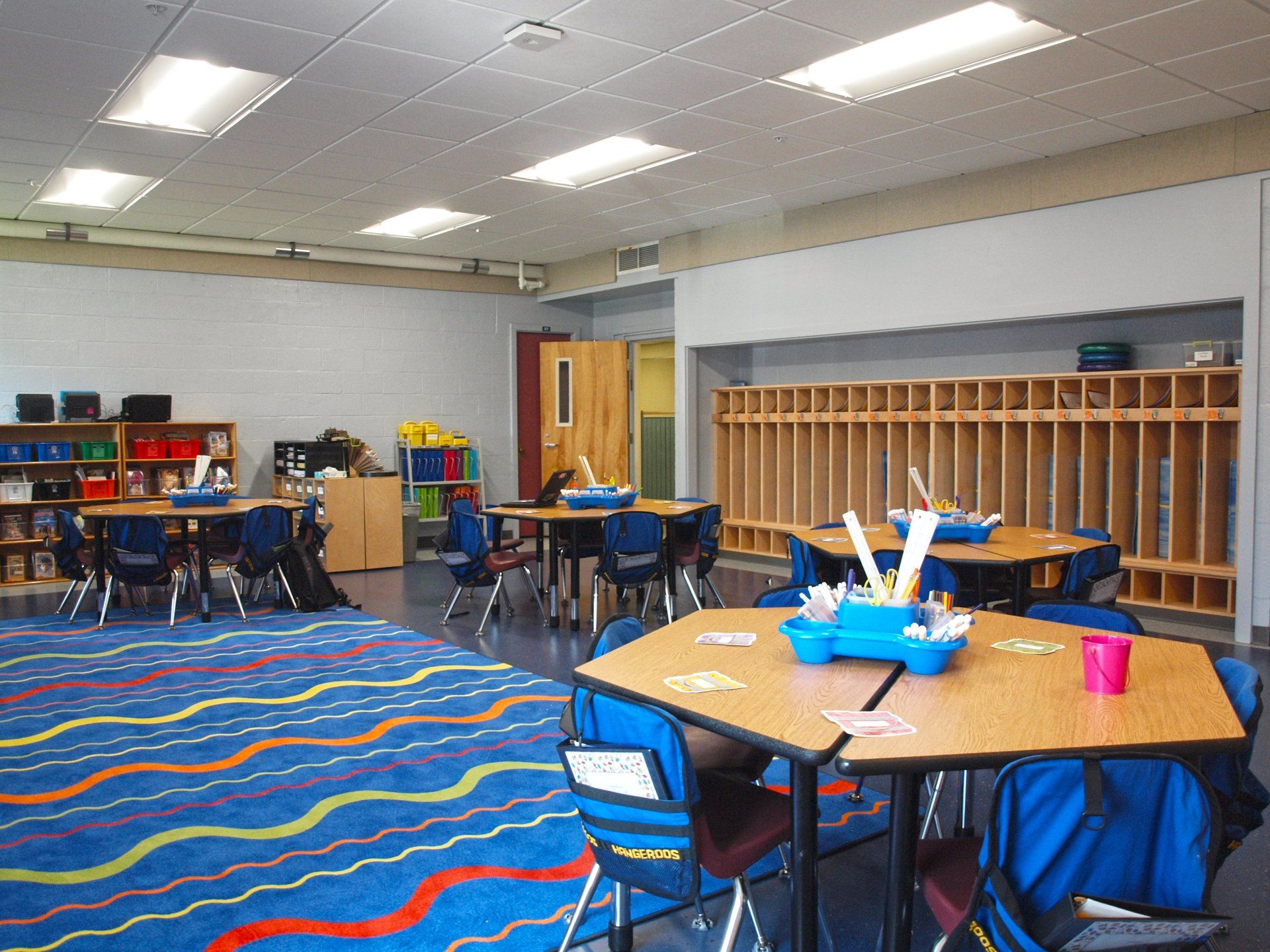 A classroom with tables and chairs and a blue rug