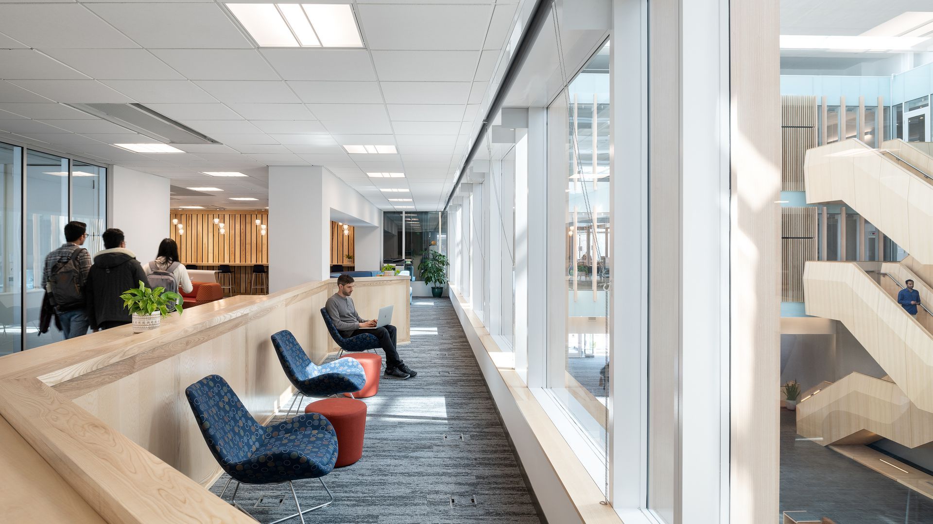 A group of people are sitting in a long hallway in a building.