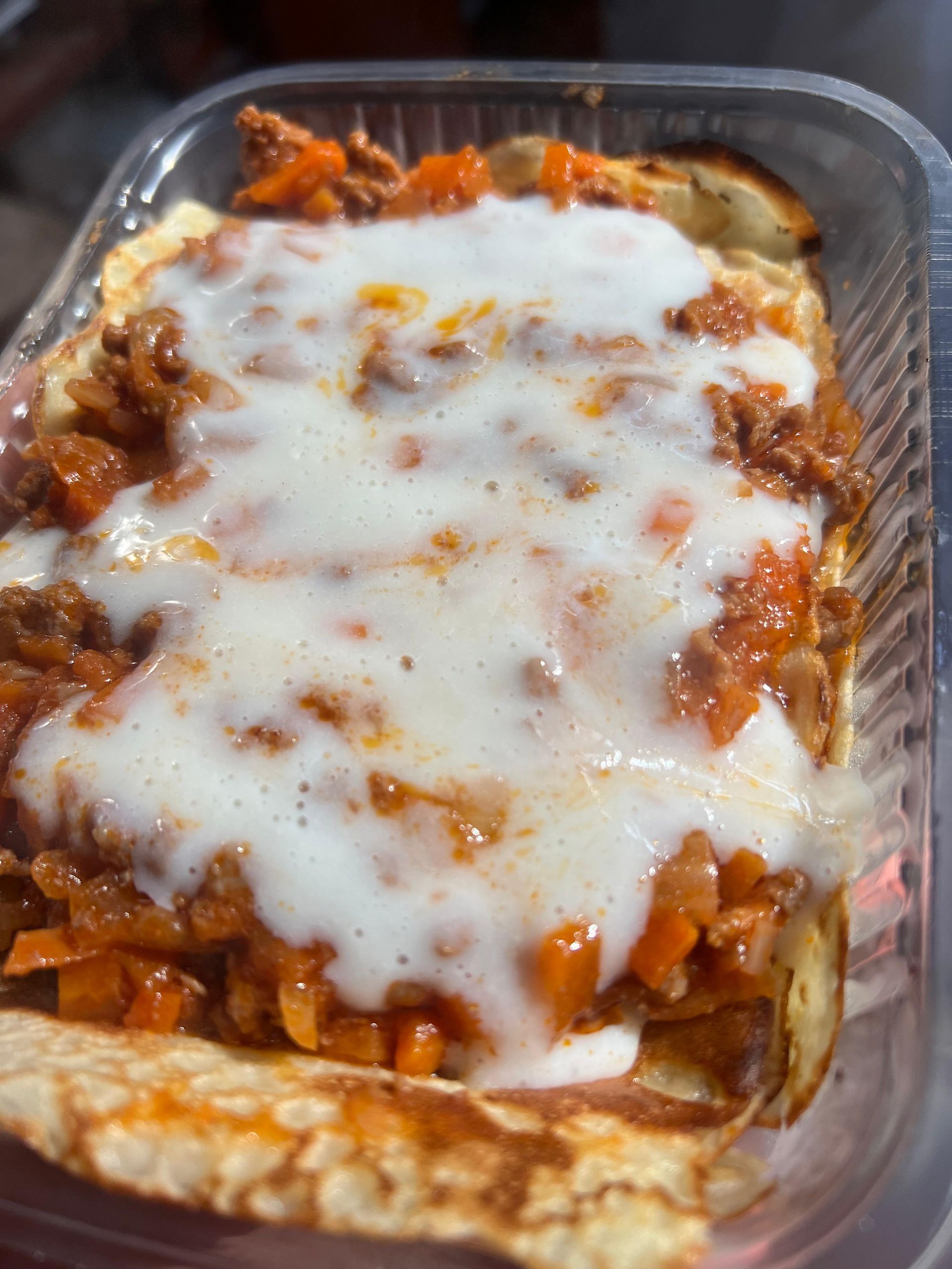 Un primer plano de una lasaña en un recipiente de plástico.