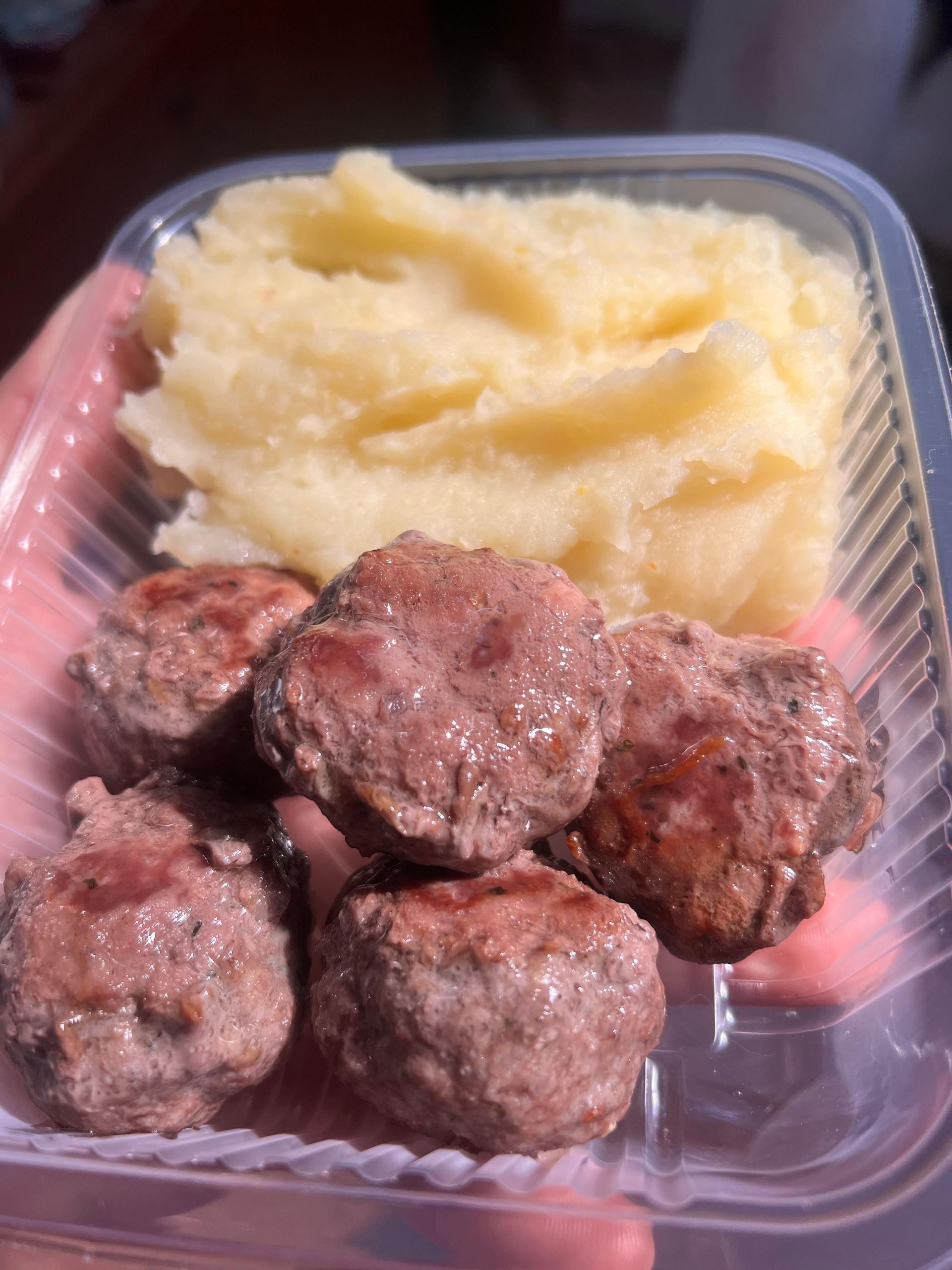 Una persona sostiene un recipiente de plástico con albóndigas y puré de patatas.