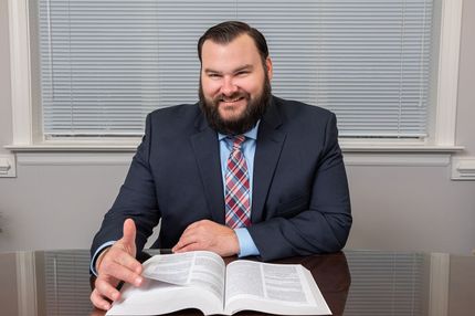 A man in a suit and tie is sitting at a desk reading a book.