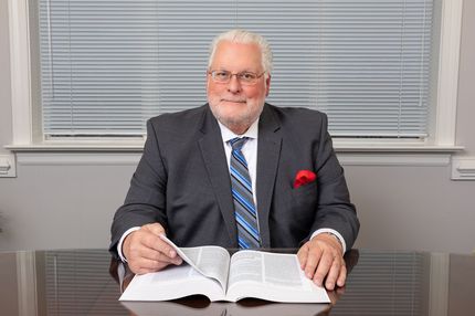 A man in a suit and tie is sitting at a desk writing in a book