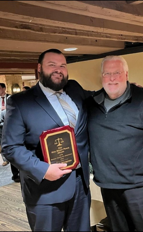 A man in a suit is holding a plaque with the letter t on it