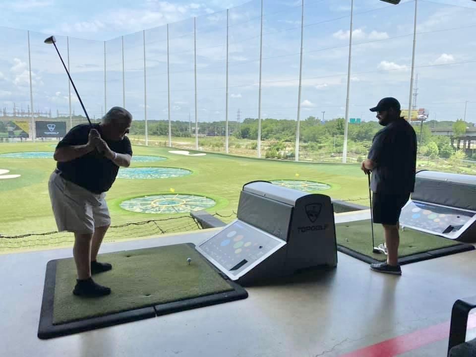 A man is swinging a golf club at a golf course while another man watches.