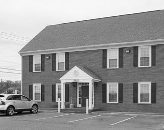 A black and white photo of a brick building with a car parked in front of it.