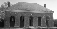 A black and white photo of a brick building with arched doors