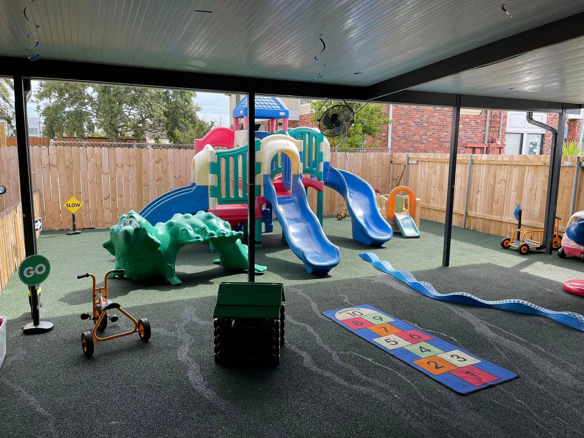 a children 's playground with a crocodile , slides , and a hopscotch mat .