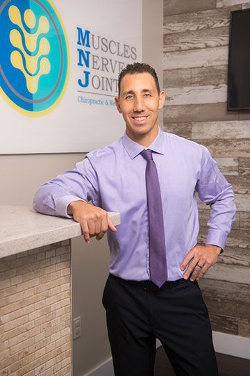 Man in lavender shirt and purple tie standing by a reception desk in a medical office lobby