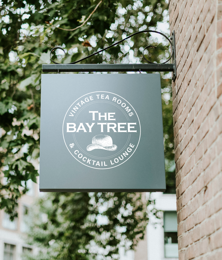 A sign for the bay tree and cocktail lounge hangs on a brick wall.