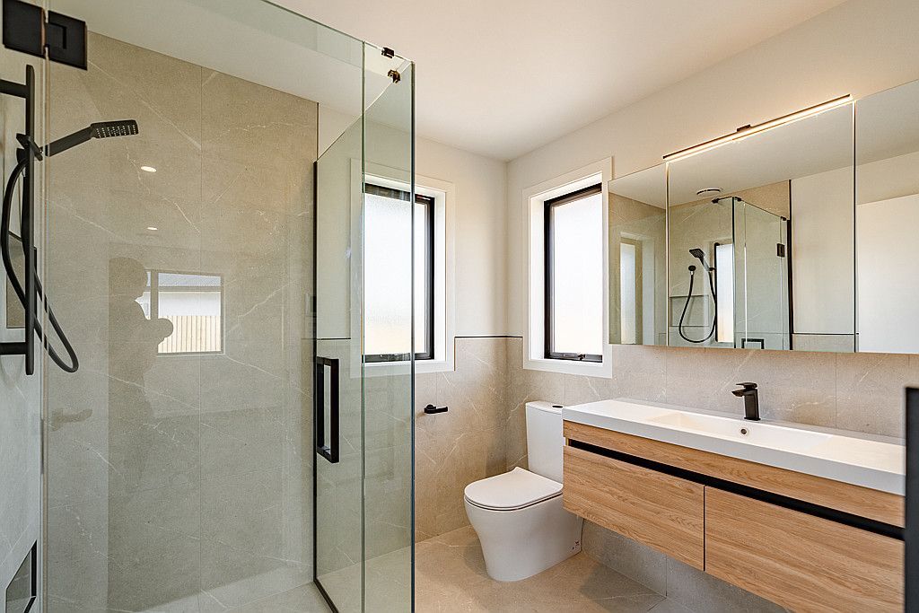 A bathroom with a toilet , sink , shower and mirror.