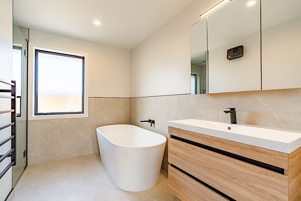 A bathroom with a tub , sink , mirror and window.