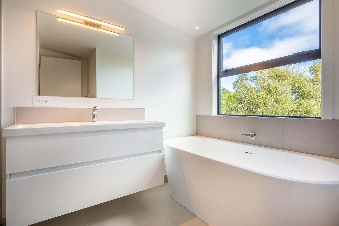 A bathroom with a tub , sink , mirror and window.