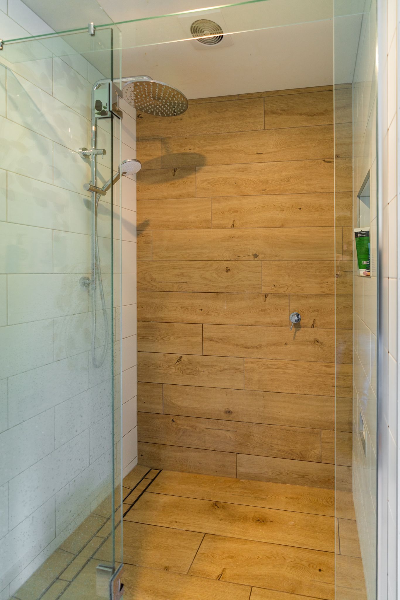 A walk in shower with a wooden wall and a glass door.