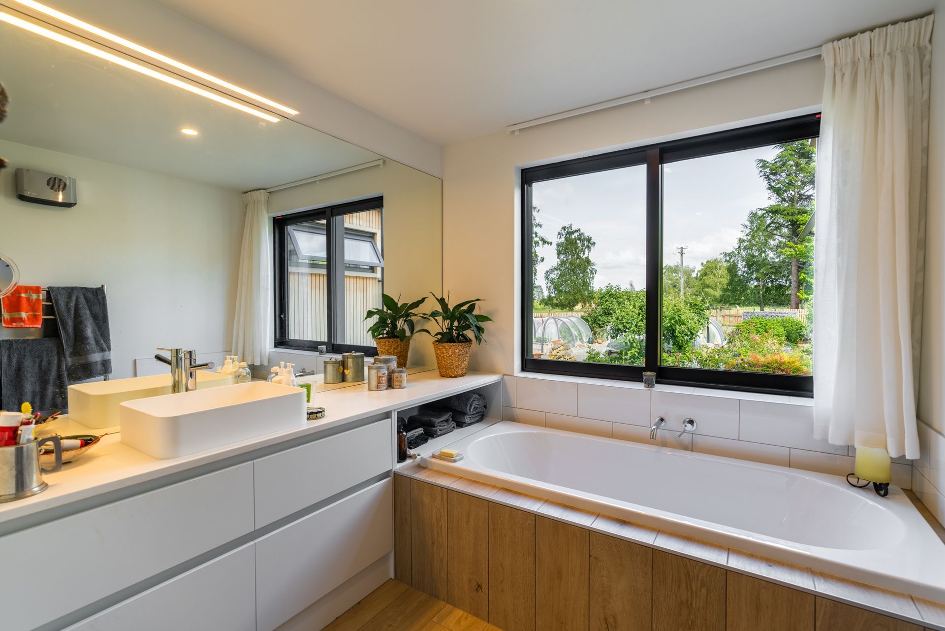 A bathroom with a tub , sink , mirror and window.