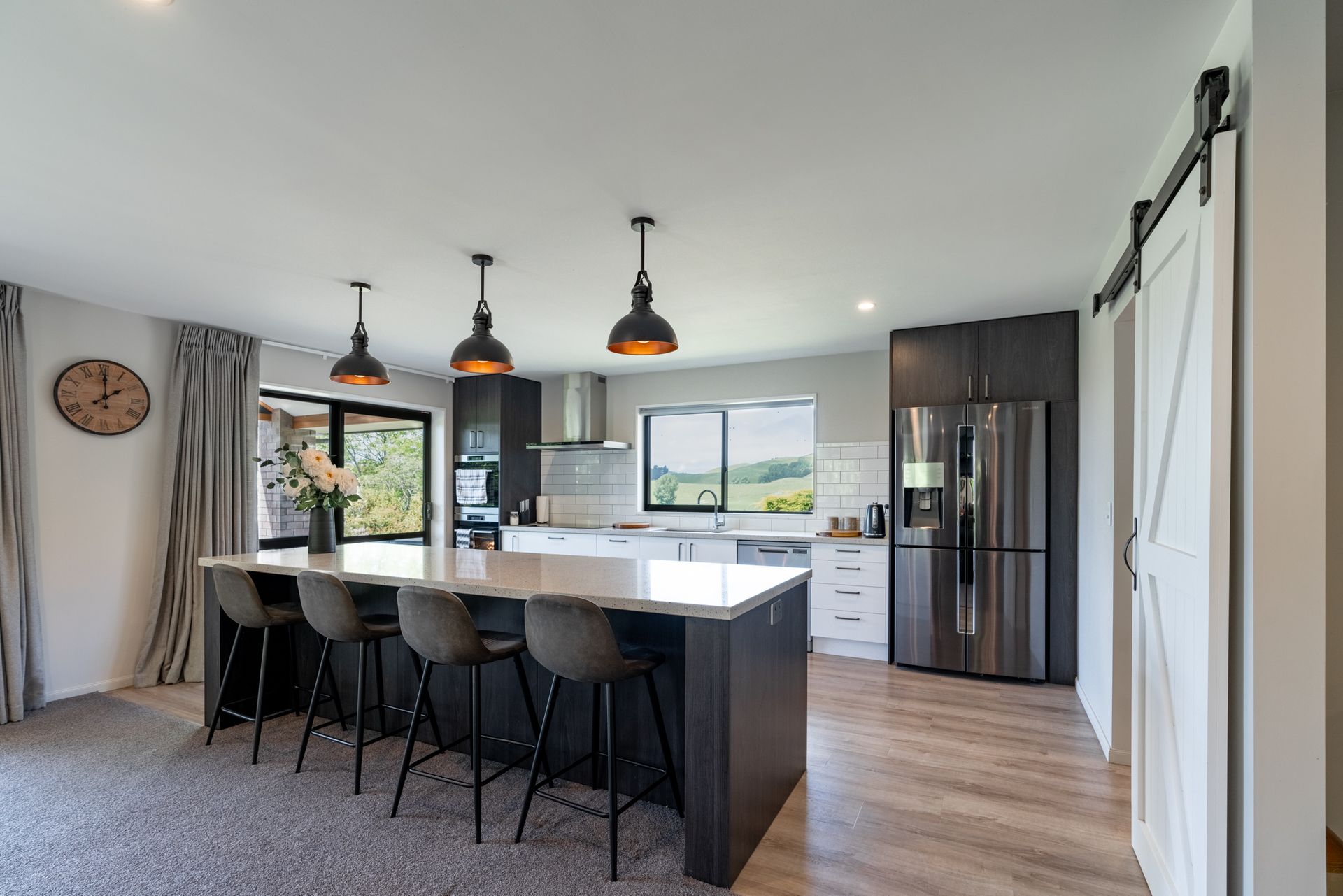 A kitchen with a large island and stools and a clock on the wall.