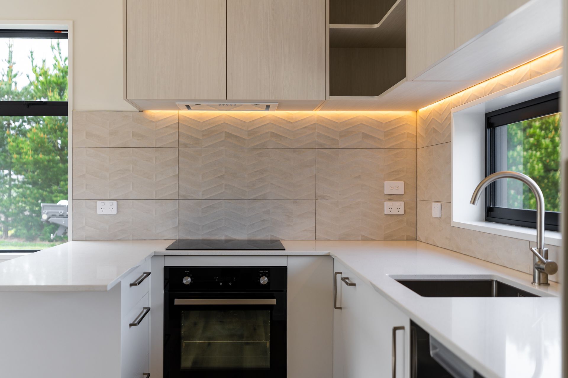 A kitchen with white cabinets , a black stove top oven , a sink , and a window.