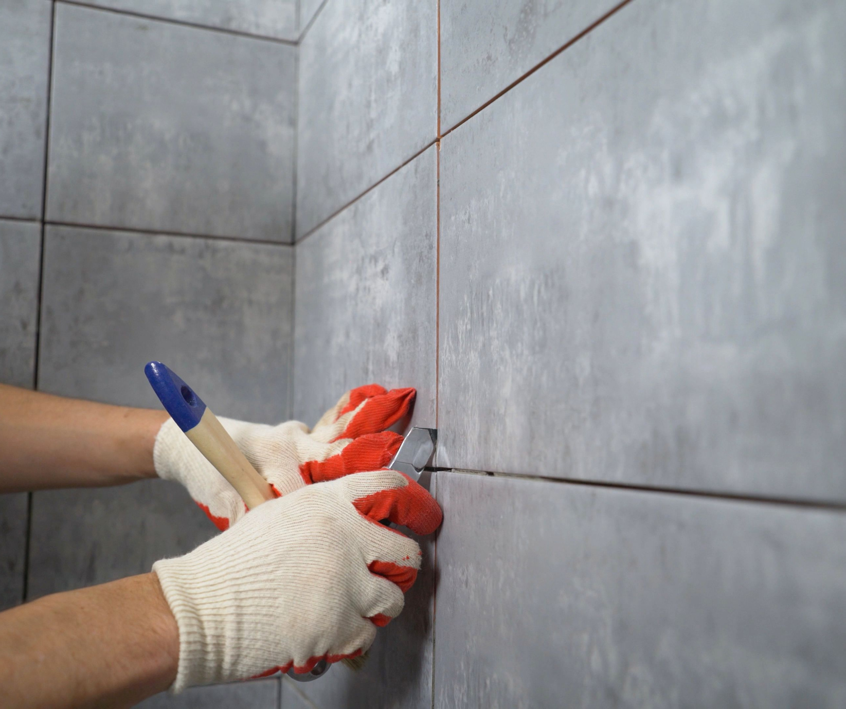 A person wearing red and white gloves is working on a tiled wall.
