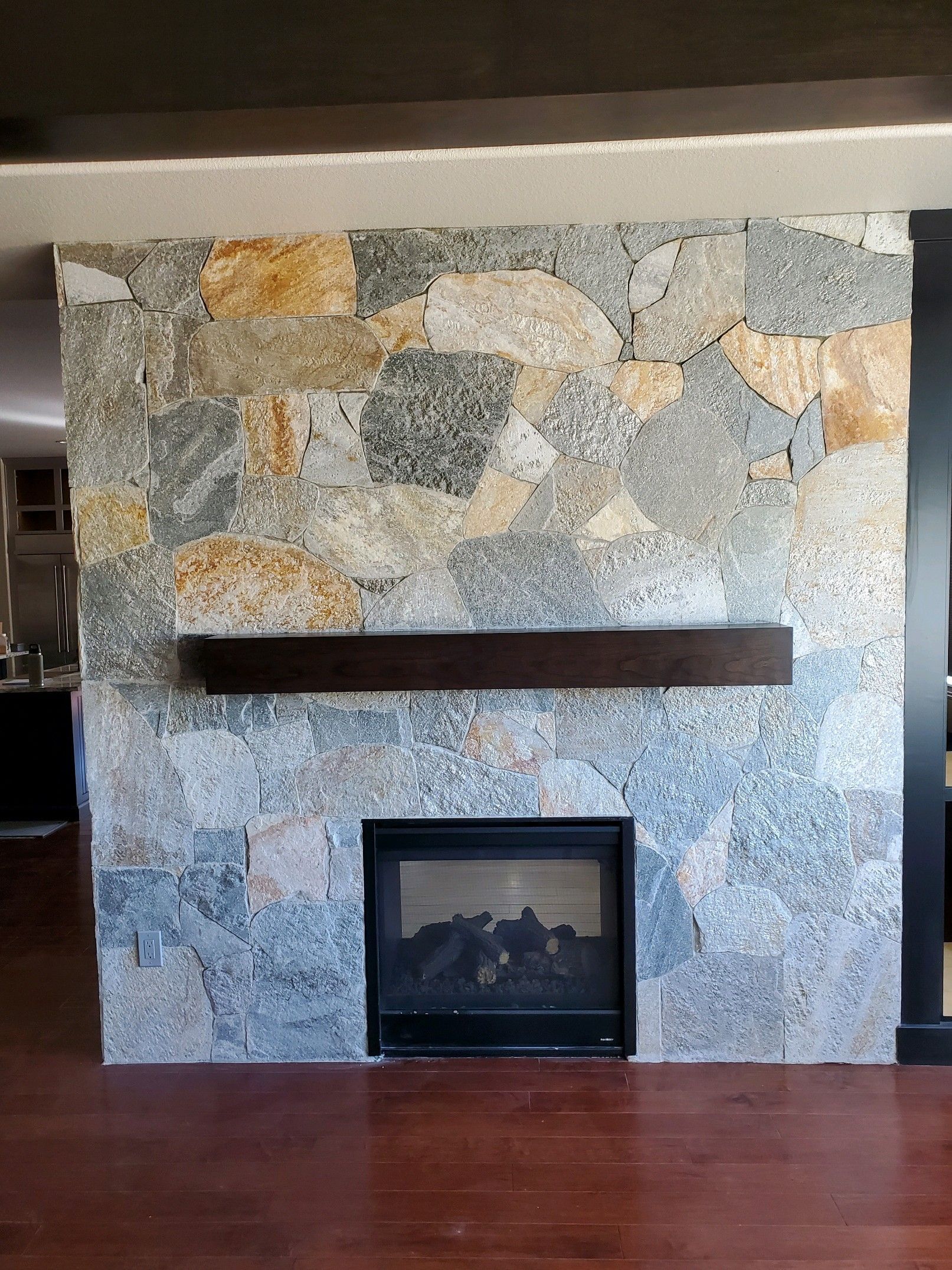 A fireplace with a stone wall and a wooden mantle in a living room