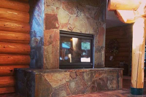 There is a fireplace in the middle of a log cabin