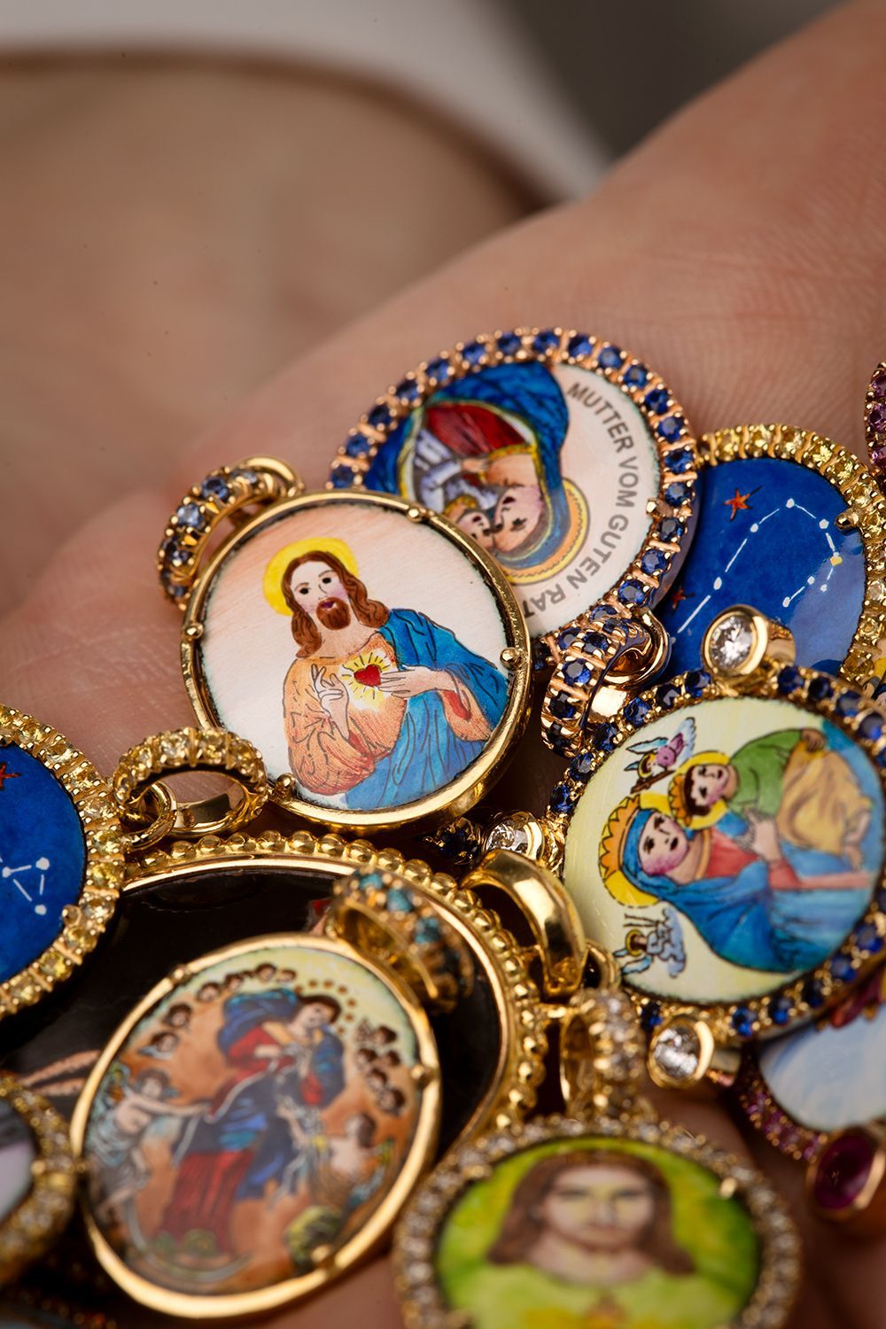 Nahaufnahme eines Armbands mit goldenen und juwelenbesetzten religiösen Medaillons, die Jesus, Maria und andere Figuren darstellen.