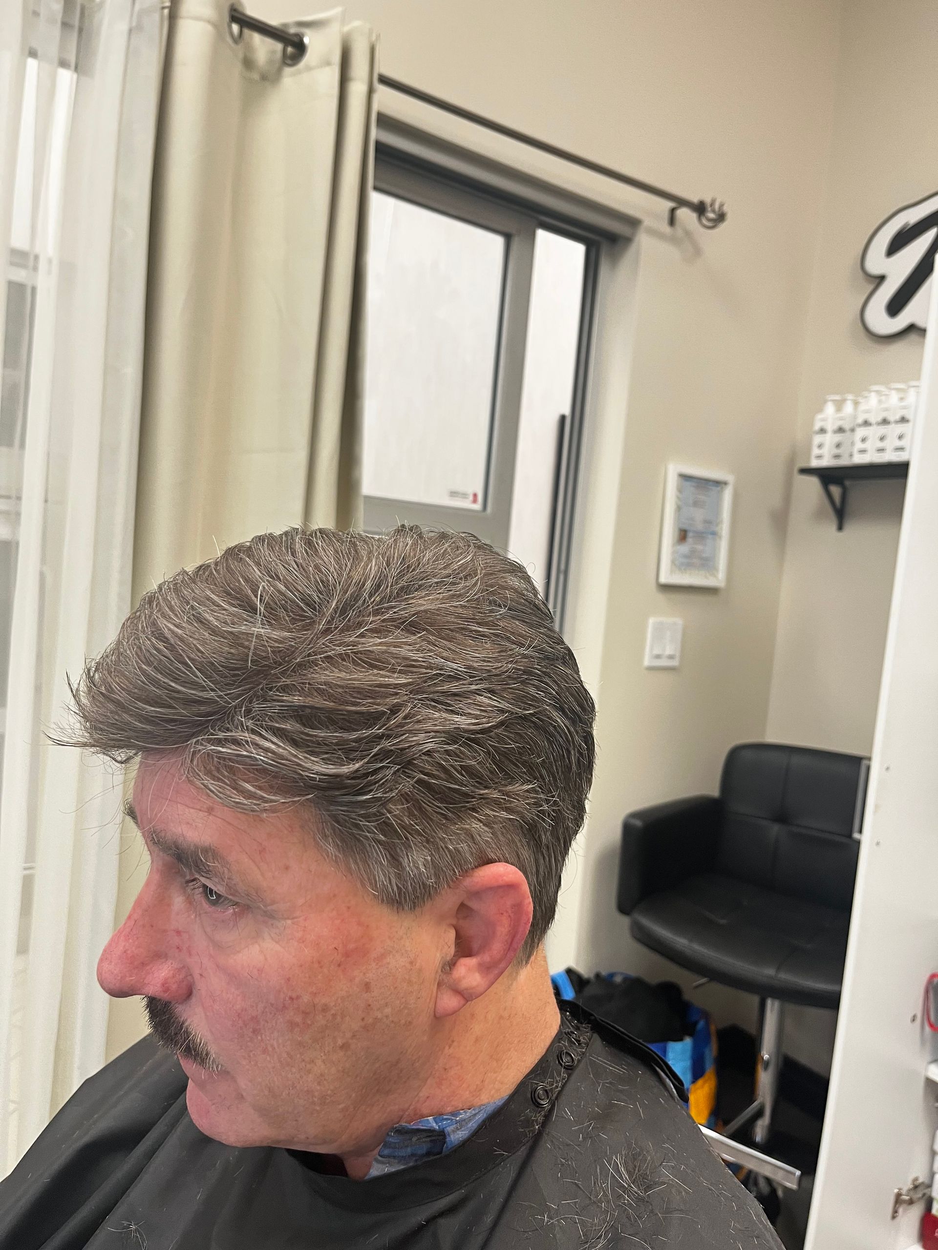 A person with short, textured hair sitting in a salon chair wearing a black barber cape.