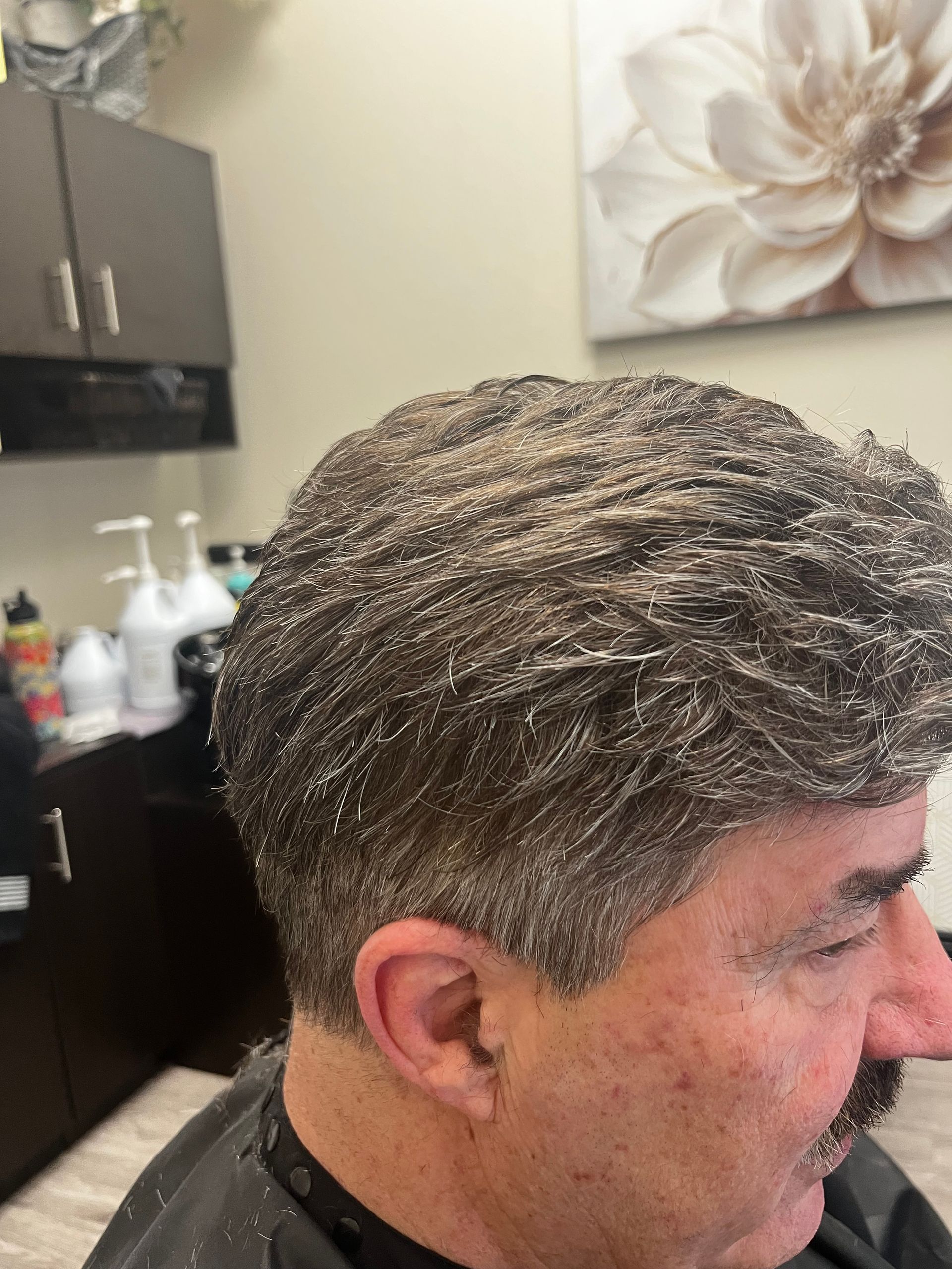 Man with thinning hair looks distressed at his reflection in a red hand mirror.