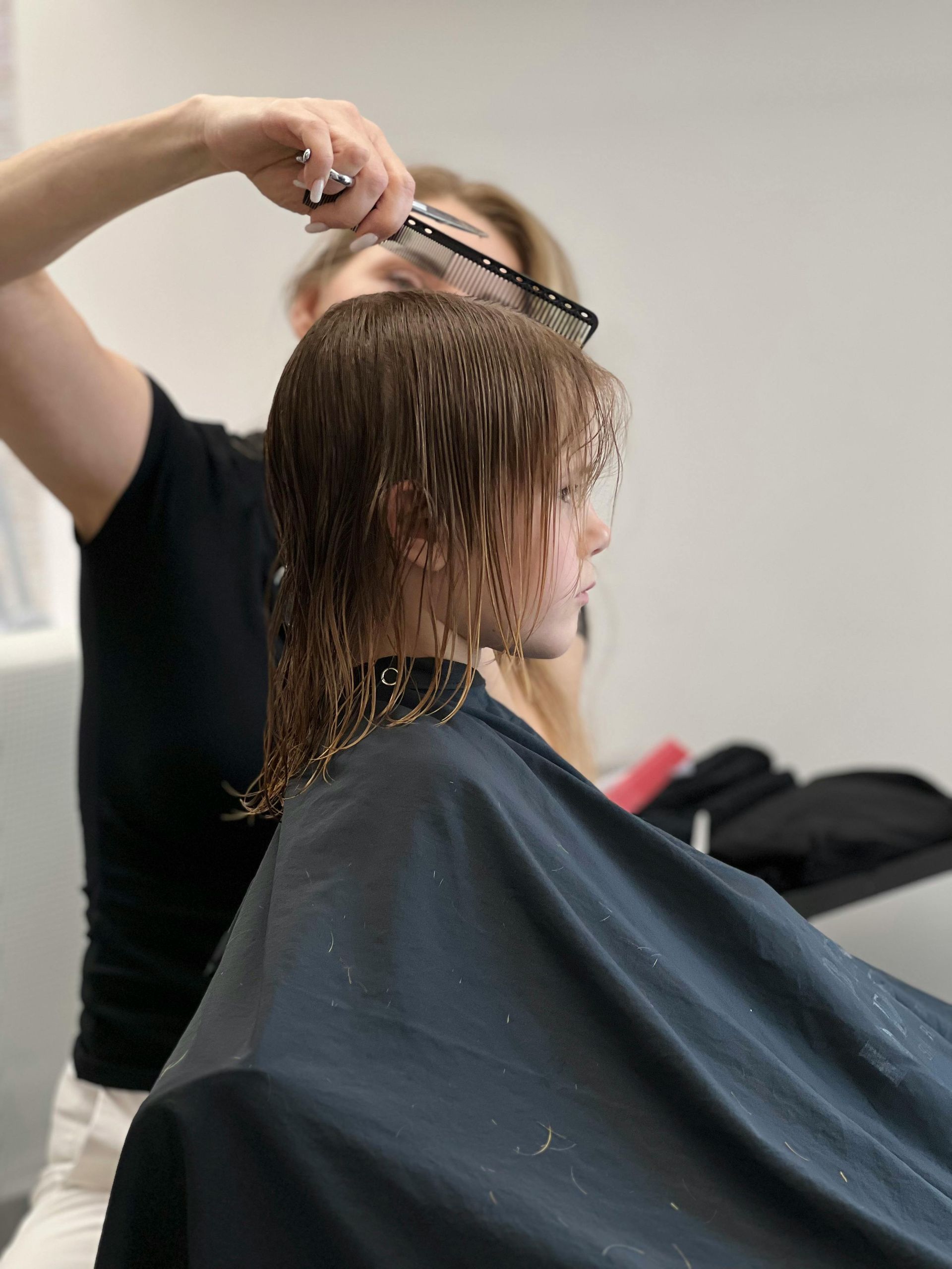 Hairdresser cutting a person's wet hair. The person is in a salon chair wearing a cape.