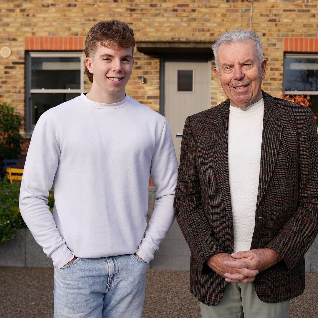 Two men standing next to each other in front of a brick building