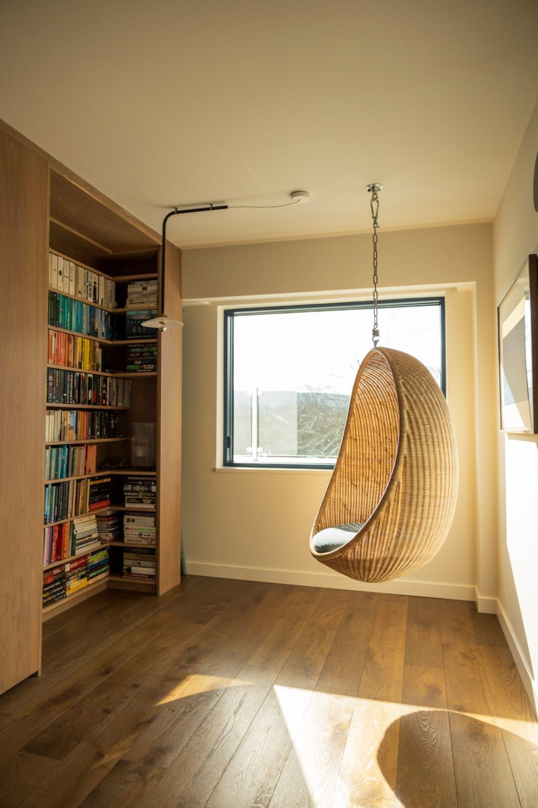 A wicker chair is hanging from the ceiling in a room next to a bookshelf.