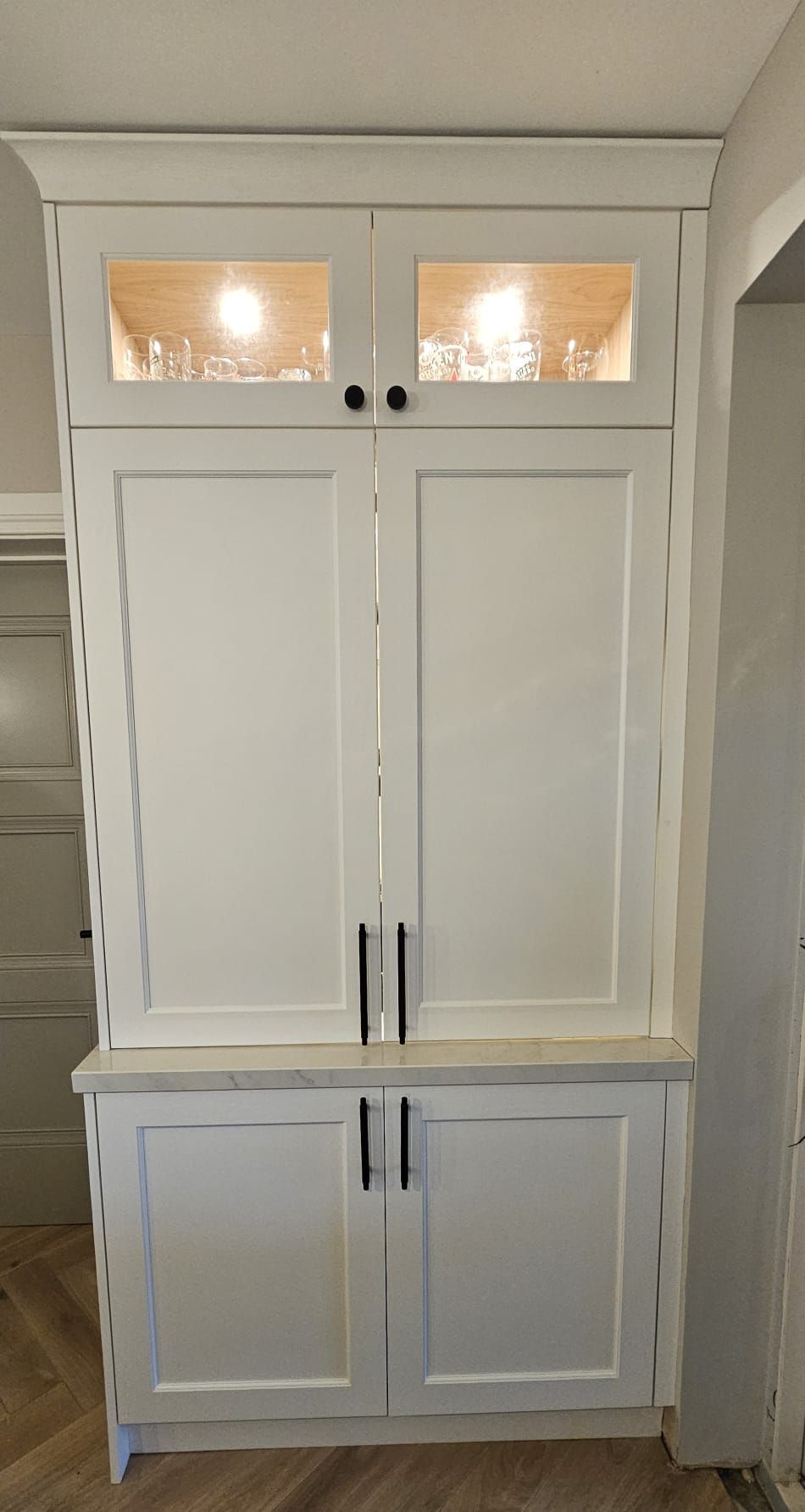A white cabinet with a glass door and a light inside of it.