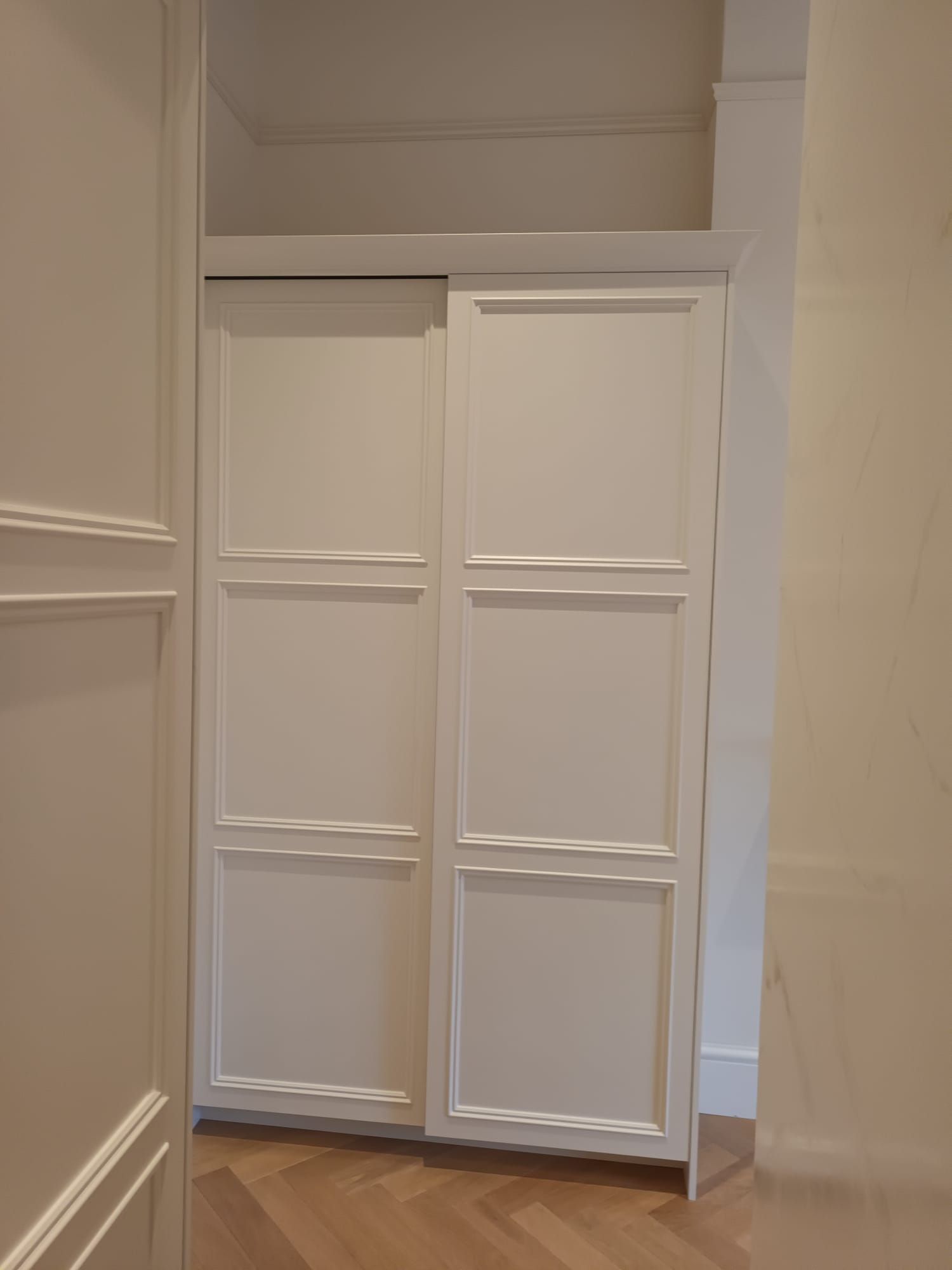 A white wardrobe with sliding doors in a hallway.
