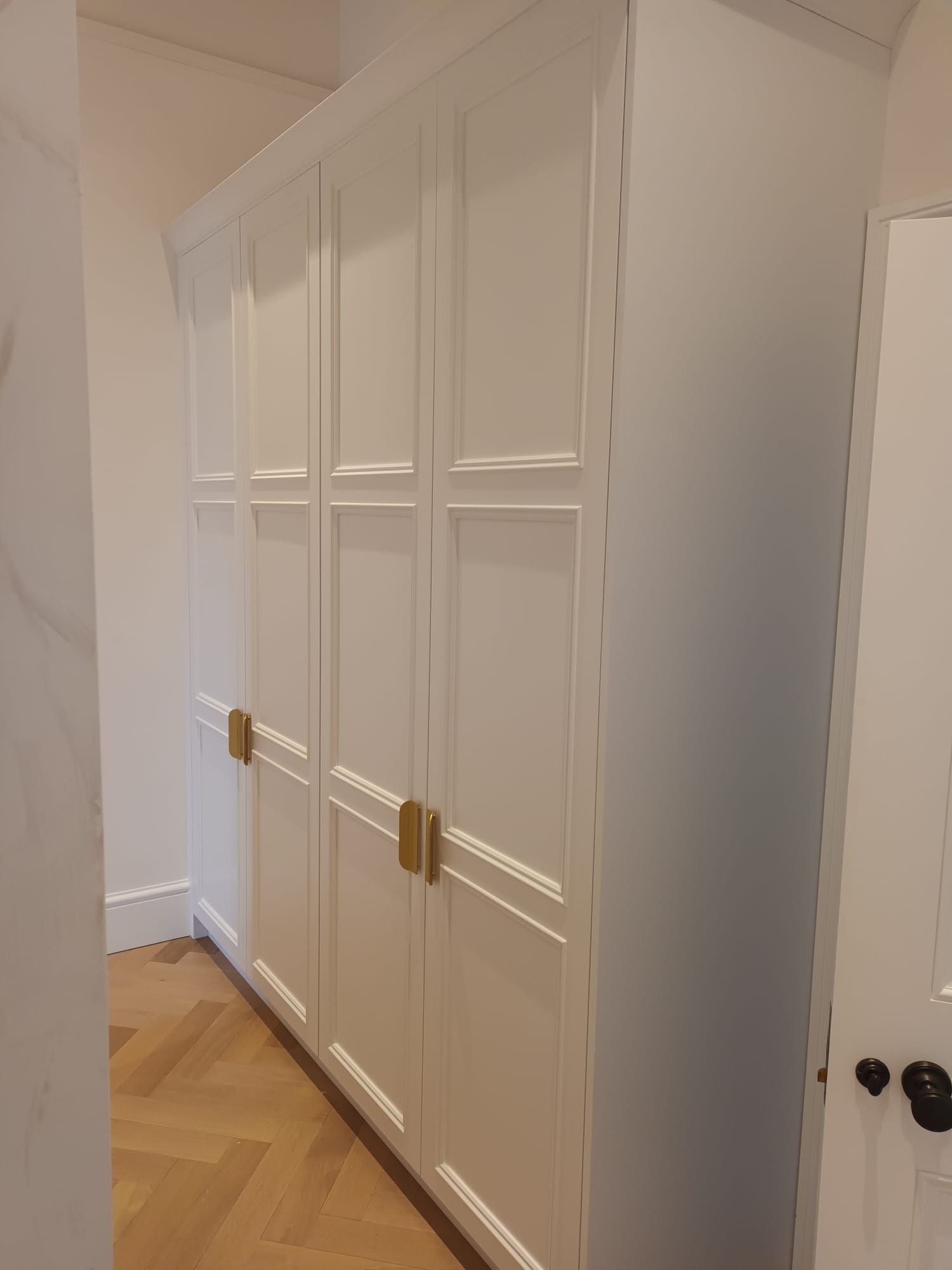 A row of white cabinets with gold handles in a hallway.
