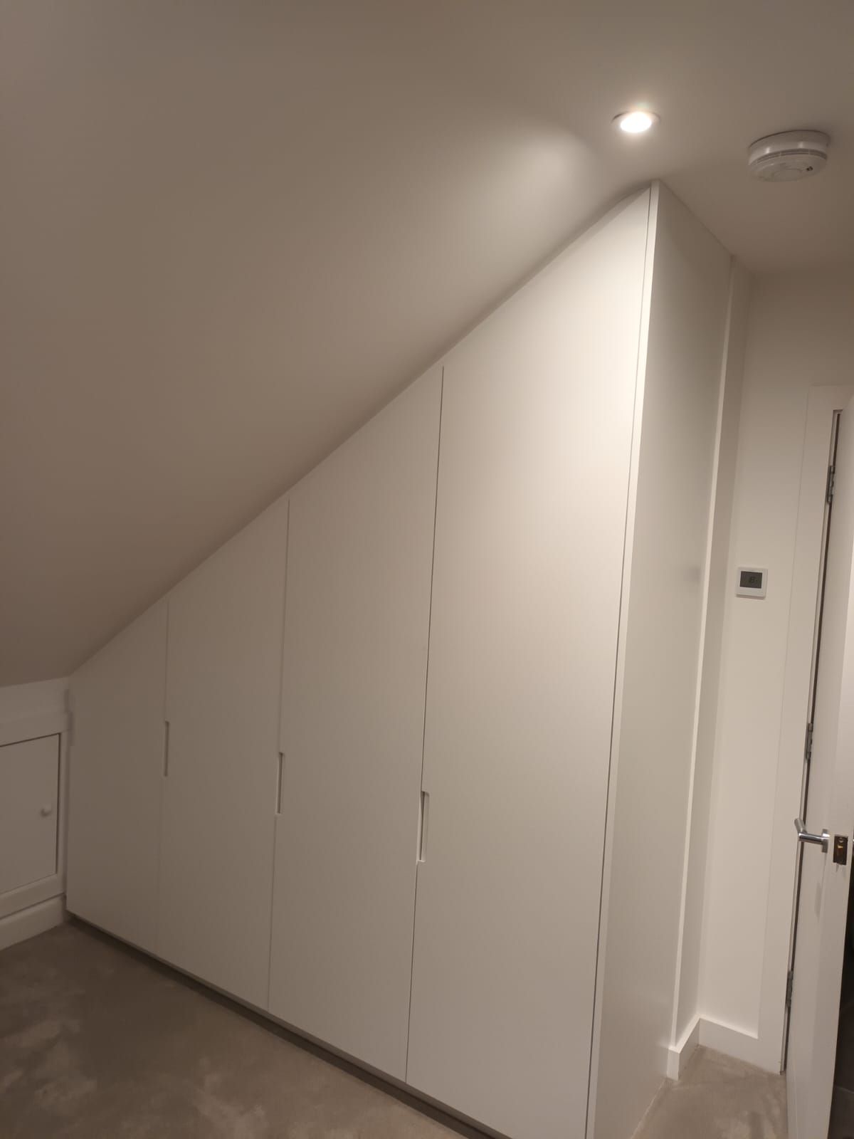 A room with a slanted ceiling and white cabinets.