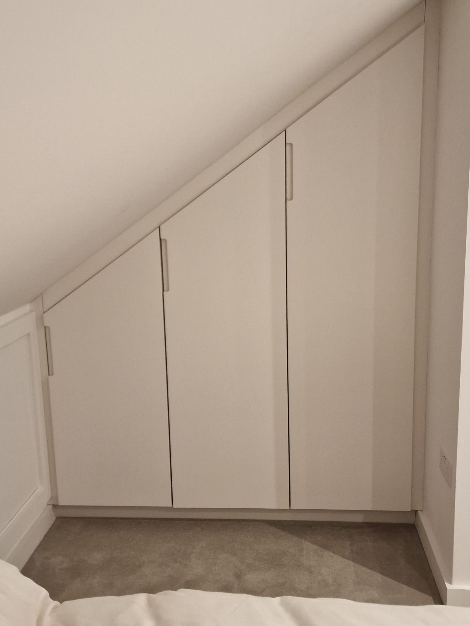 A bedroom with a slanted ceiling and white cabinets underneath it.
