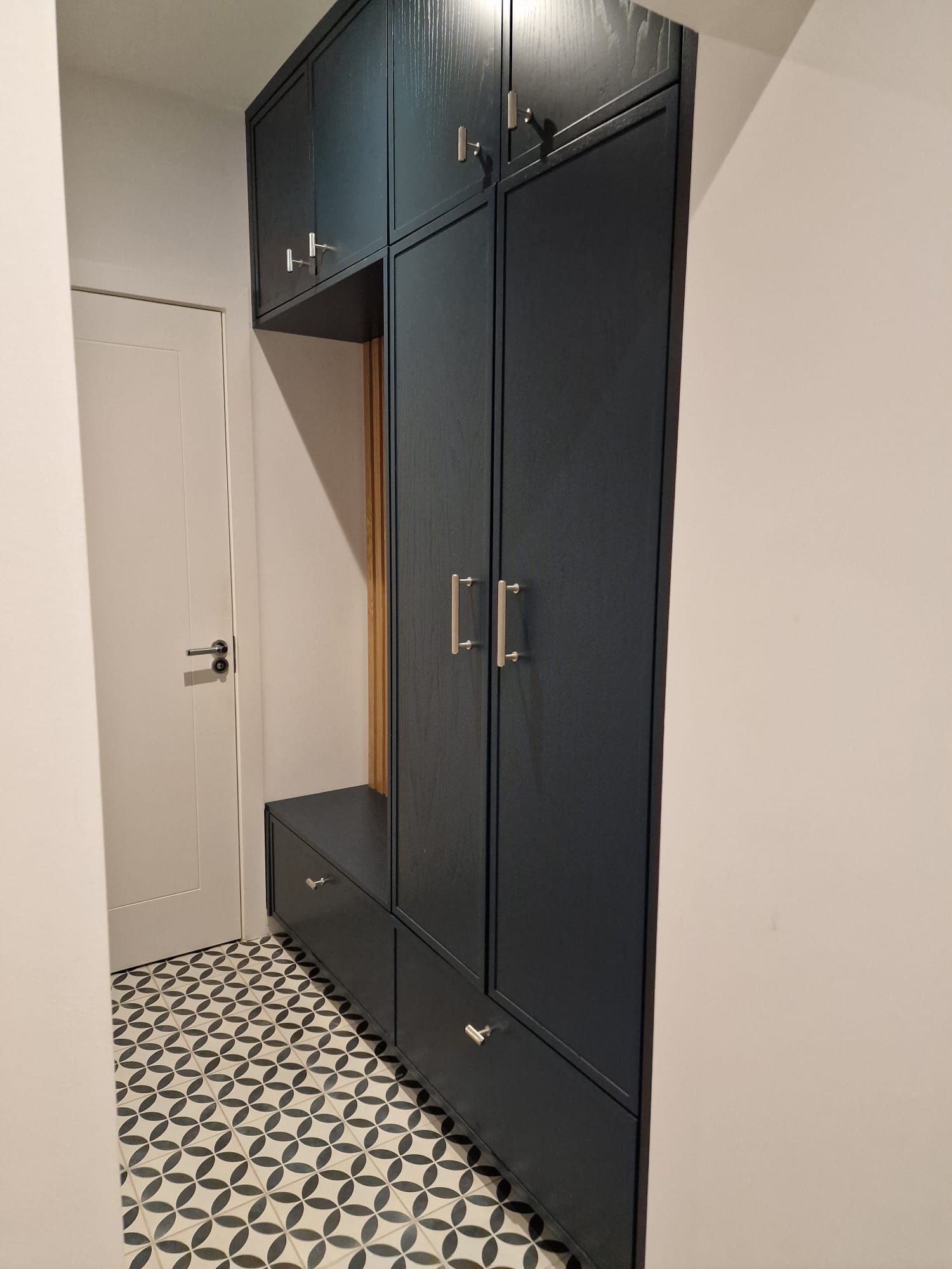 A hallway with blue cabinets and drawers and a black and white tile floor.