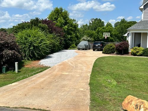 Concrete driveway leads to vehicles, with grass and landscaping on either side under a blue sky.