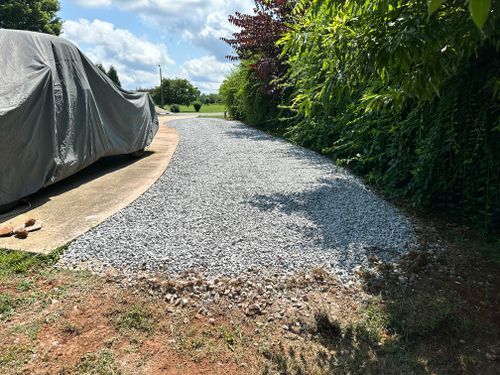 A gravel driveway next to a green hedge and a vehicle covered in a gray tarp.