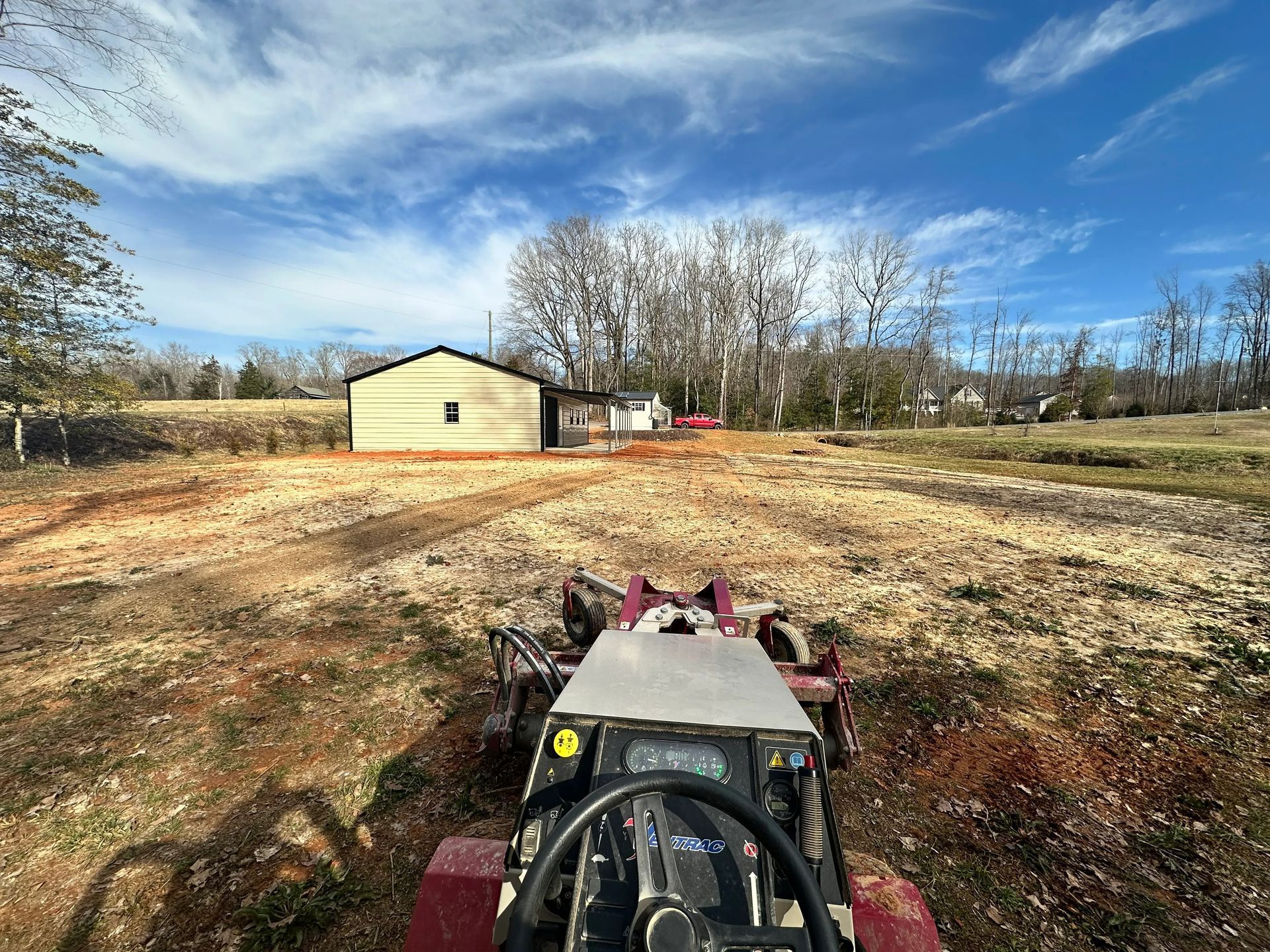 Tractor in field, facing shed and trees on a sunny day.