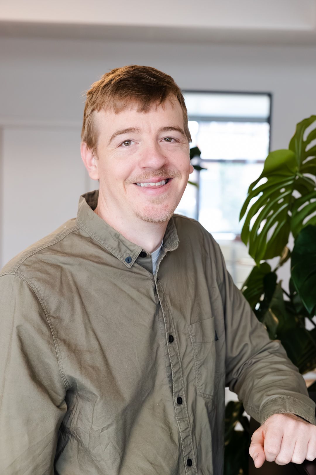 En mand i en grøn skjorte står foran en plante og smiler.