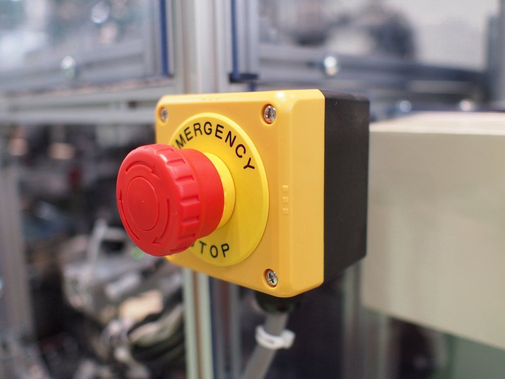 Bouton d'arrêt d'urgence rouge sur boîtier jaune, monté sur machine.