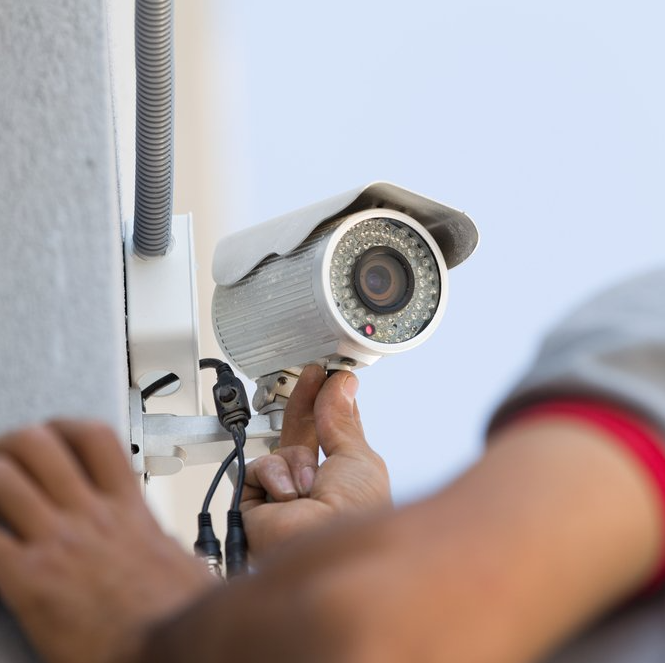Personne installant une caméra de sécurité à l'extérieur d'un bâtiment.