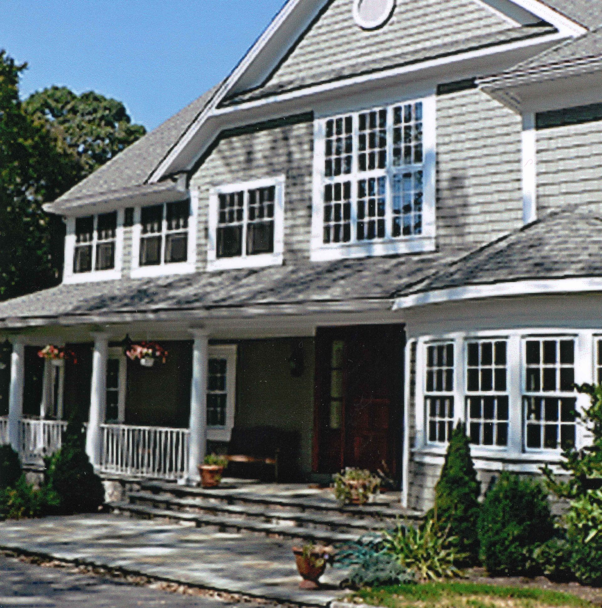 Gray shingled house with porch, multiple windows, and a landscaped yard.