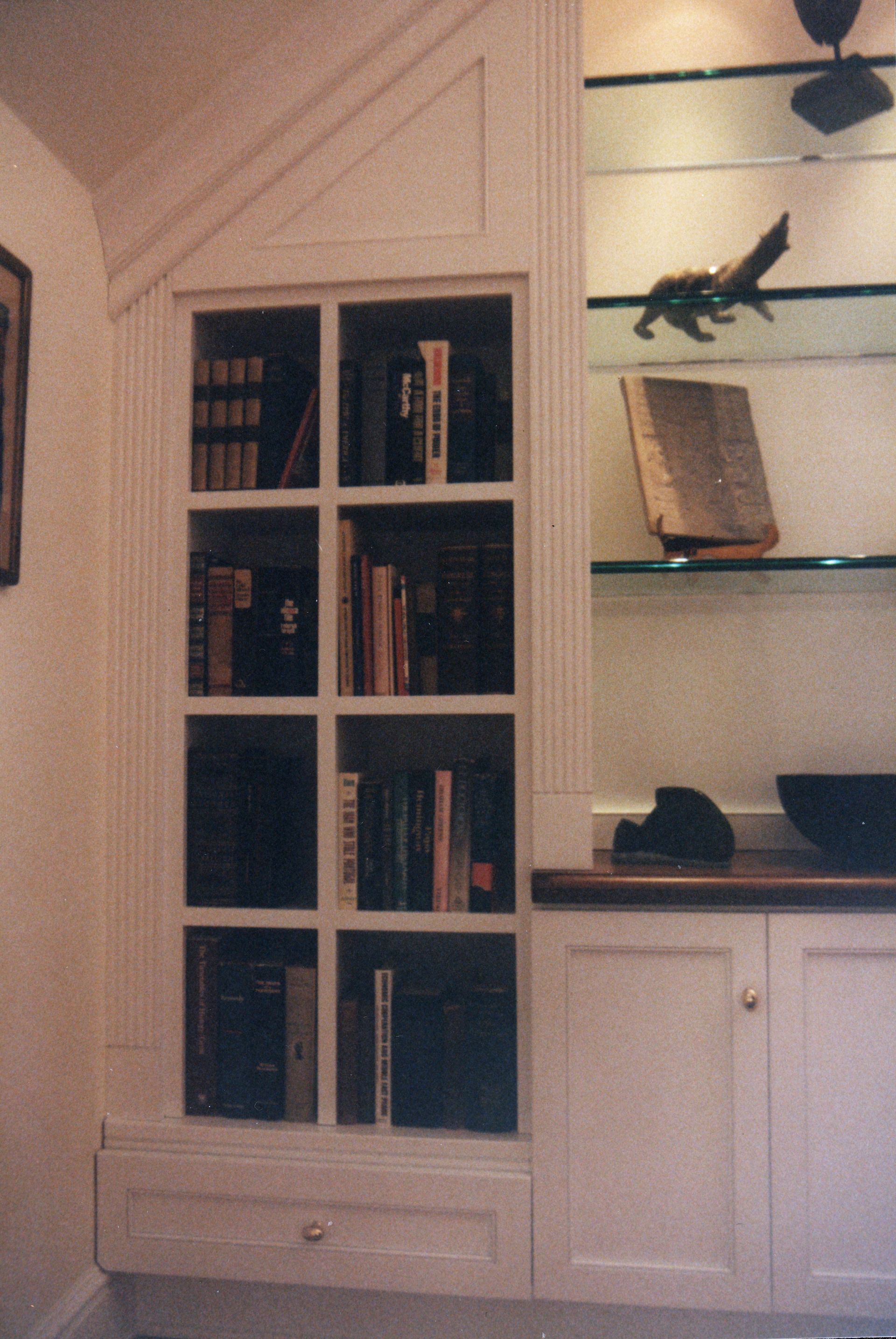 Built-in white bookcase with books and glass shelves, and a drawer at the bottom.