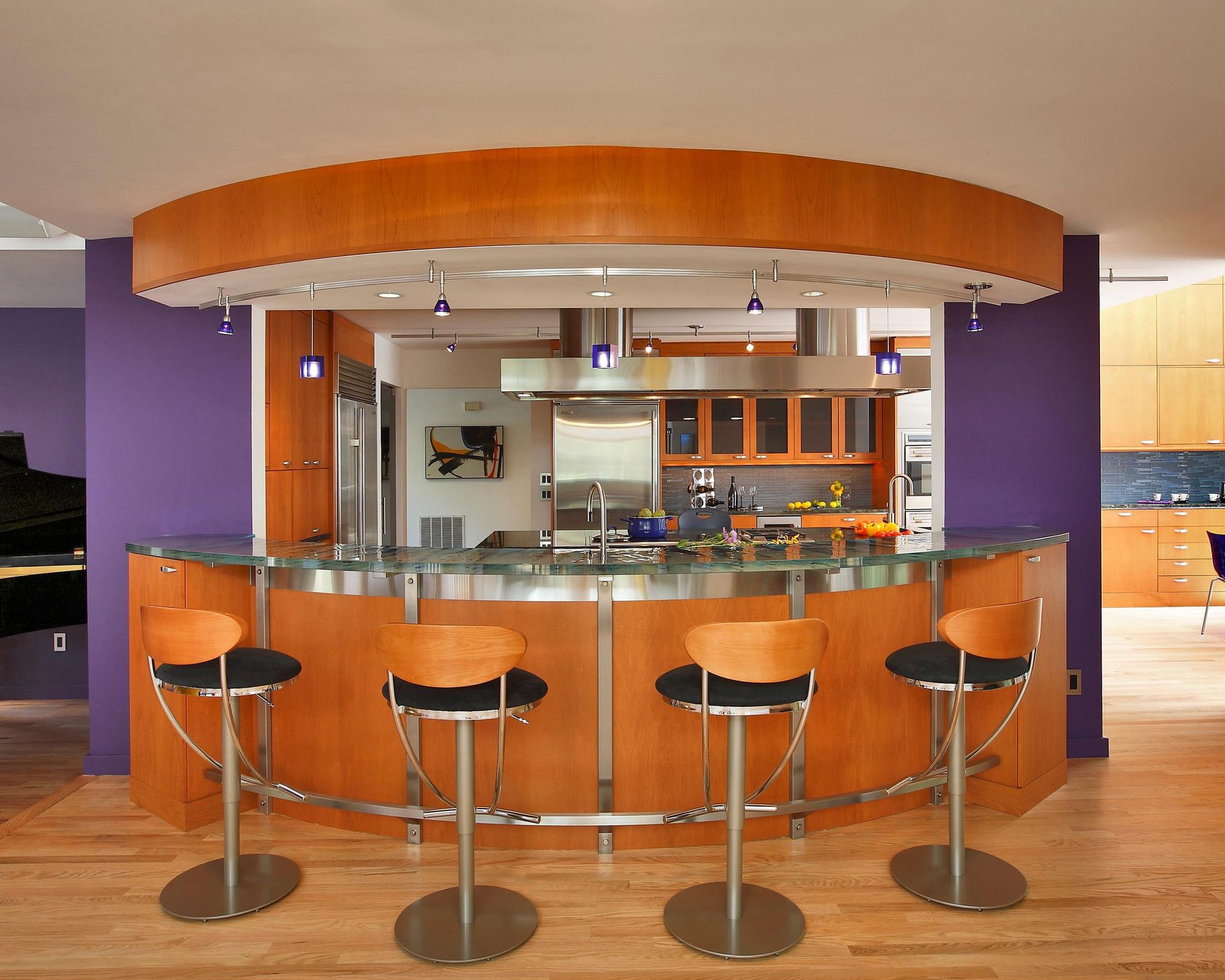 Curved kitchen bar with wood and metal accents, purple walls, and bar stools.