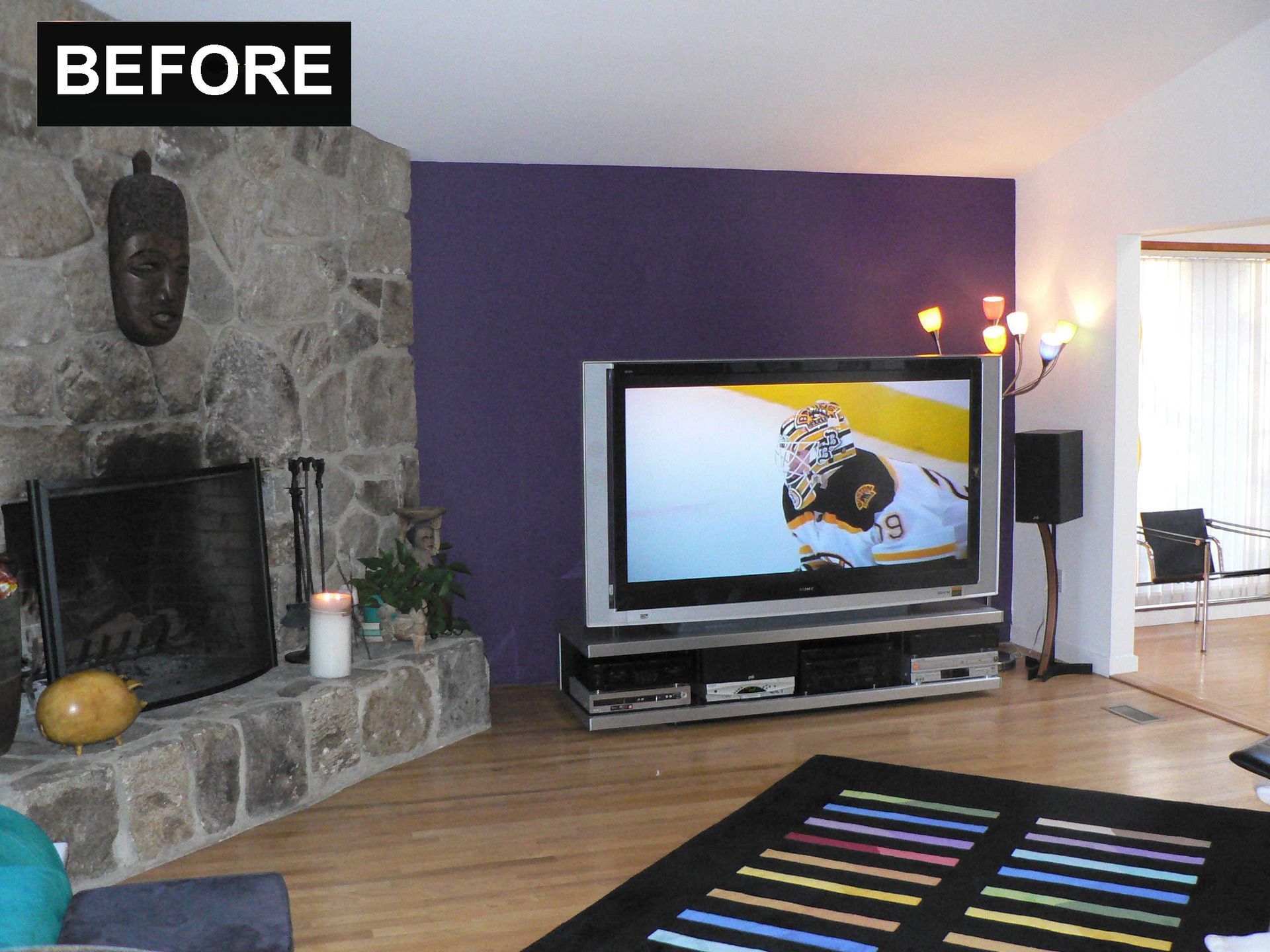 Living room before renovation with purple wall, stone fireplace, and TV.